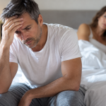 Hombre preocupado por impotencia sexual mientras su pareja permanece al fondo